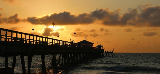 A Florida dock stretching out above the ocean at sunset.