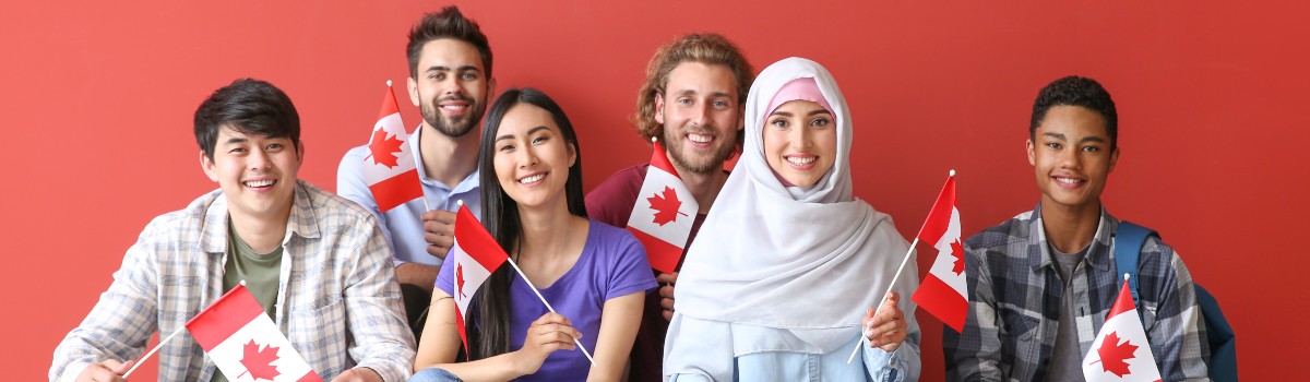 A group of six young people with diverse ethnic backgrounds smile widely while holding small Canadian flags.