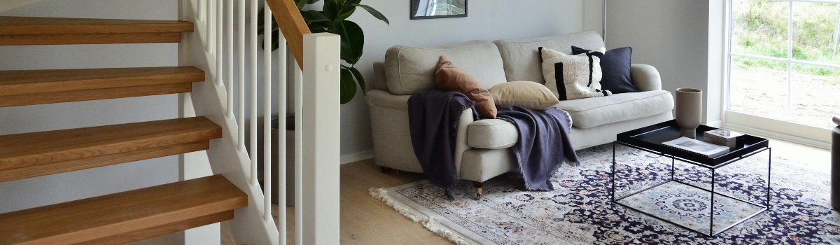 A staircase leading to a living room containing a sofa, filled with four pillows and a throw, a Persian-style rug, and a coffee table.