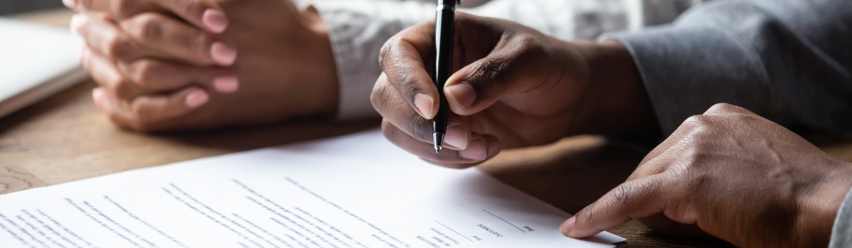 A witness sits next to a person signing a legal document.